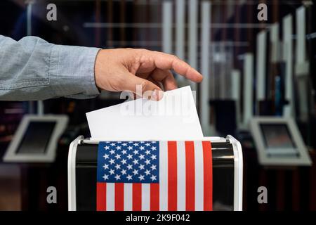 Election in USA. Man putting his vote into ballot box and American flag on background, closeup Stock Photo