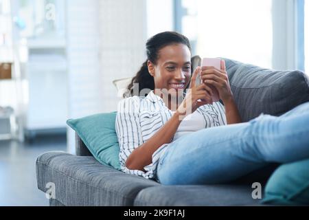 Scrolling through all her social media channels. a young woman texting on a cellphone at home. Stock Photo