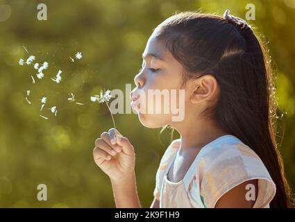 Spring, freedom and girl blowing dandelion flowers for hope, growth and environment in park. Happy, light and health with child wish on plant in peace Stock Photo