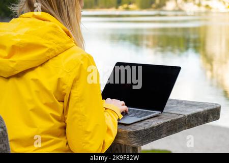 Remote worker relaxing near the lake and using a laptop. Working or studying over a laptop and smartphone. Stock Photo
