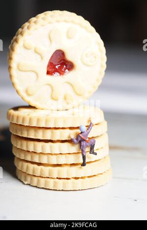 Photograph of Miniature man climbing the Jam biscuit mountain, a stack of jammie biscuits with a heart in and a miniature person half way up the pile. Stock Photo