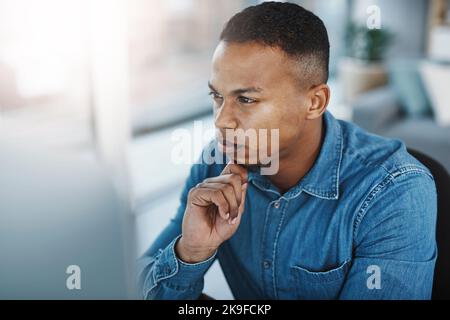 I wonder what else I can add to this proposal. a young businessman looking thoughtful while staring at his computer screen in a modern office. Stock Photo