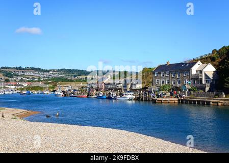 Fishing boats and yachts moored along the River Axe in the harbour with buildings and countryside to the rear, Axmouth, Devon, UK. Stock Photo