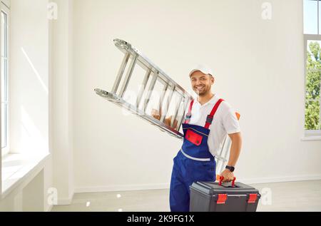 Happy repairman standing in the room, holding a ladder and a toolbox and smiling Stock Photo