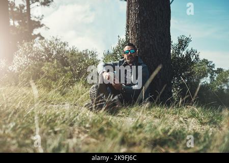 I think this spot has the best connection out here. Full length portrait of a middle aged man sitting by a tree and using his cellphone. Stock Photo