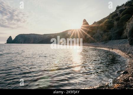 A red burning sunset over the sea with rocky volcanic cliff. Abstract nature summer ocean sea background. Small waves on golden warm water surface Stock Photo