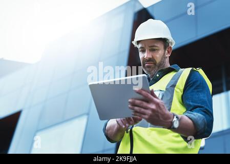 Architects tend to wear many different hats. a engineer using a digital tablet on a construction site. Stock Photo