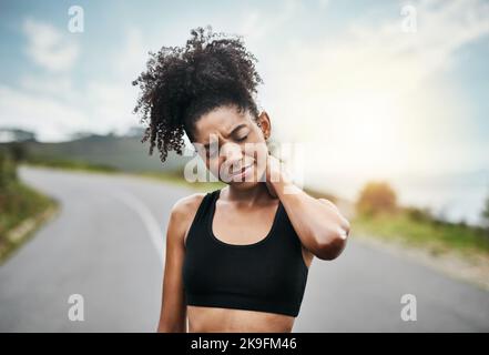 I should have stretched some more. a sporty young woman holding her neck in pain while exercising outdoors. Stock Photo