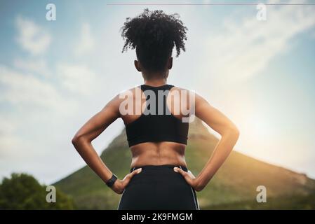 The road ahead...Rearview shot of an unrecognizable young sportswoman standing with her hands on her hips outside. Stock Photo