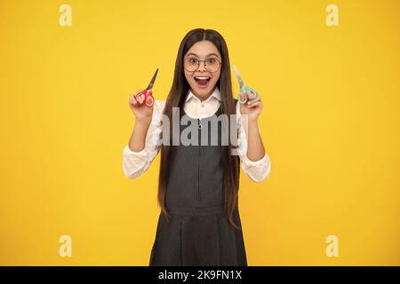 Excited amazed teenage girl with scissors, isolated on yellow background. Child creativity, arts and crafts. Stock Photo