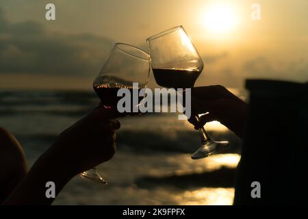 Close-up silhouette of two glasses of wine clinking against the background of the sea at sunset. Concept of celebration, romance, friendship Stock Photo