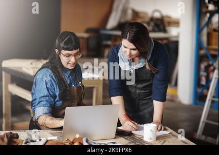 Come take a look at this. two attractive young creative female artisans working on a laptop in their workshop. Stock Photo