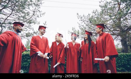 happy graduates laughing and celebrating graduation on college campus. Education, success and modern youth concept. Stock Photo