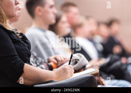 Female hands holding pen and notebook, making notes at conference lecture. Event participants in conference hall. Stock Photo