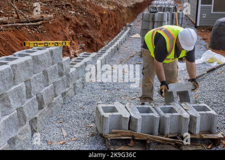 Construction site worker installing newly constructed large block retaining wall construction near new home Stock Photo