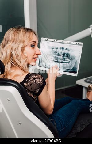 The patient sits in the dentist's chair and holds an X-ray of the teeth Stock Photo