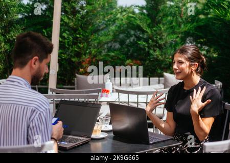 Two young businesspeople having conversation in cafe bar on a summer day, view from side, close up shot Stock Photo