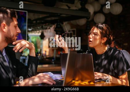Two stunning business partners are having a conversation about their project, at restaurant's terrace, on a sunny day Stock Photo