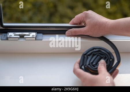 a woman glues a sealing rubber tape on a window in a living room. Stock Photo
