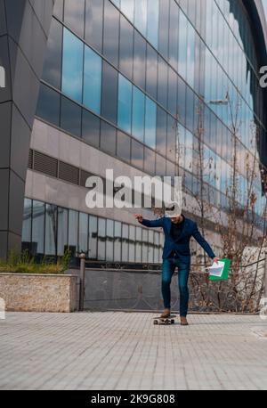 Full length of an attractive smiling young businessman wearing suit, carrying folder while riding skateboard Stock Photo