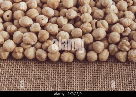 Roasted hazelnuts on a background of burlap. Scattered Heap of nut kernels. Copy space for text. Close-up. Stock Photo
