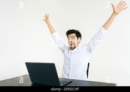 Studio shot of smiling excited young man looking at laptop screen, feeling amazed by getting email with good news at desk on white isolated background Stock Photo