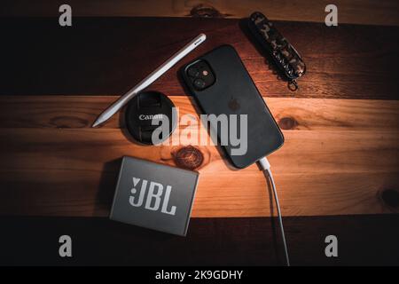 A top view of an iPhone next to a JBL speaker, Apple pencil, Canon camera lens cover, and a jackknife. Stock Photo