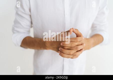 Close-up cropped shot of unrecognizable stressed man ins casual shirt racking knuckles and fingers feeling nervous on white background. Stock Photo