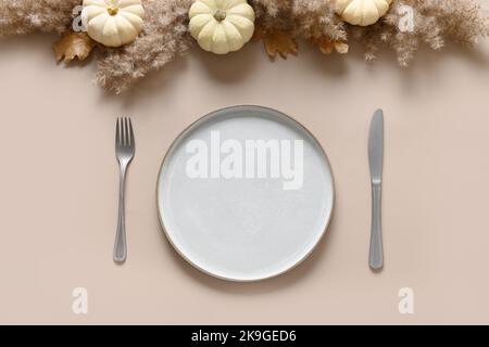 Thanksgiving day autumn table setting decoration in natural colors white pumpkins and orange berries on beige background. Top view. Copy space. Stock Photo