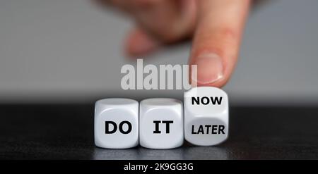 Hand turns dice and changes the expression 'do it later' to 'do it now'. Stock Photo
