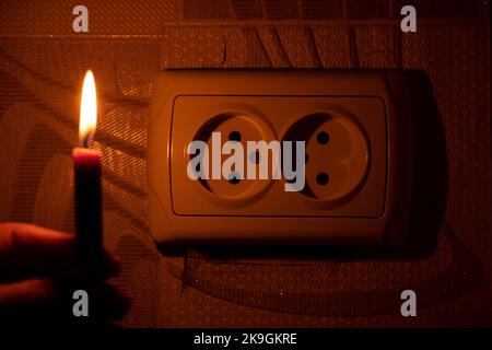 Female hand with a candle near the socket on the wall in the apartment in the dark, Ukraine, lack of light due to the war, power outages Stock Photo