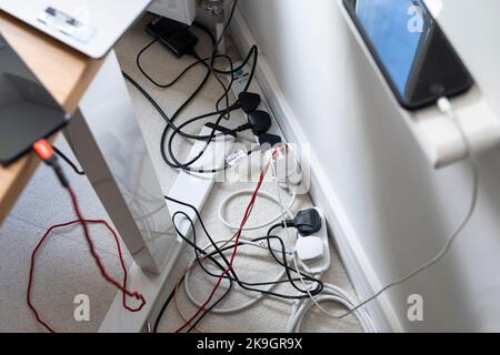 A proliferation of cables from laptop computers, a monitor and smartphones charging, all plugged into an extension adaptor. Working from home, UK Stock Photo