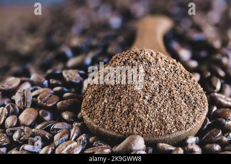 Abstract of a wooden spoonful of ground coffee over a layer of fresh roasted coffee beans. Extreme selective focus on center with blurred foreground a Stock Photo
