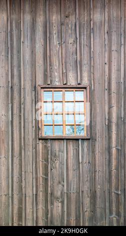 A small window with muntins against the background of a wall covered with wooden boards in a vertical arrangement. Stock Photo