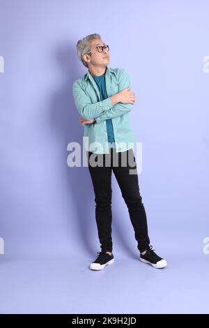 The full length of senior Asian man standing on the purple background. Stock Photo