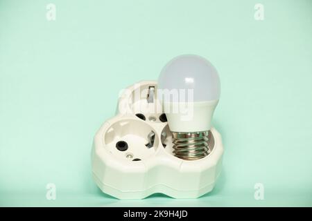 The LED light bulb lies in a triple socket on a blue background, saves electricity and light in the house Stock Photo