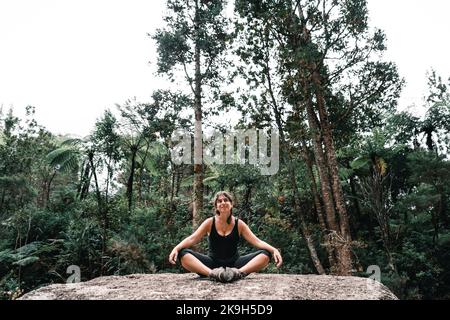 disheveled blue eyed caucasian girl smiling looking up at the sky sitting on a large rock with her arms resting on her knees in the forest on donut Stock Photo