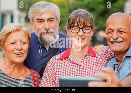 Elderly couples taking selfie with smartphone - Old friends reunion having fun outdoors with each other Stock Photo