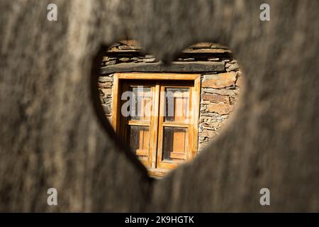 Door with a heart shaped small hole with a wooden window in the  background Stock Photo