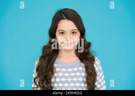 She is really cute. Happy girl child blue background. Small child wear long wavy hair. Little child with cute smile. Beauty salon. Fashion and style Stock Photo