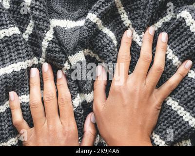 Woman's hands on gray knitted sweater with white stripes. Folded warm clothing. Crumpled textile background. Stock Photo