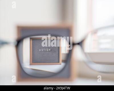 Grey letterboard with word Autism. View through eyeglasses on medical diagnosis which usually made in childhood. Stock Photo