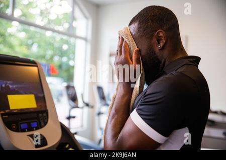 Guy in the gym wipes the sweat off with a towel after running on the treadmill Stock Photo
