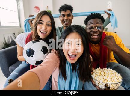 Excited multiracial young friends taking selfie while watching football on TV Stock Photo