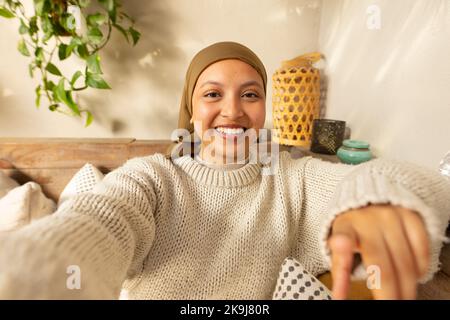 Happy biracial woman wearing hijab, having a video call Stock Photo