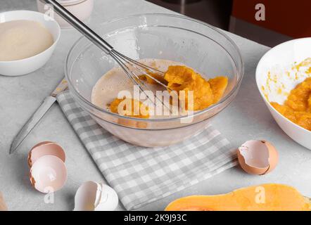 Bowl with pumpkin pie filling and whisk with ingredients for baking a pie on a gray table in the kitchen Stock Photo