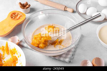 Bowl with pumpkin pie filling and whisk with ingredients for baking a pie on a gray table in the kitchen Stock Photo