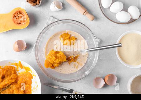 Bowl with pumpkin pie filling and whisk with ingredients for baking a pie on a gray table in the kitchen Stock Photo