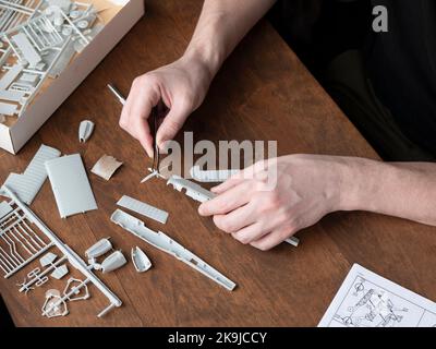 Person is assembling several small pieces to make the final aircraft model. Parts of plastic model airplane in man's hands, selective focus Stock Photo