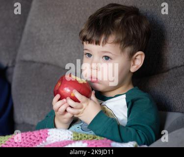 young boy eating apple on the couch Stock Photo